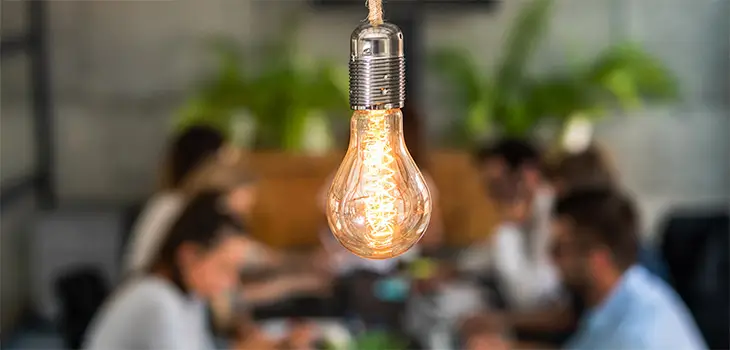 Lightbulb in forefront with couple sitting at restaurant table out of focus in background.