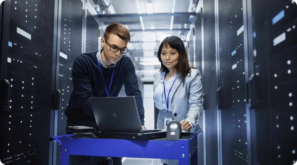 2 people in a server room looking at a laptop