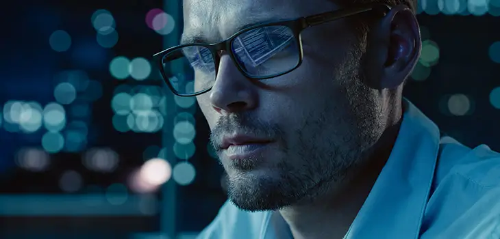 IT worker wearing glasses looks at screen with blinking lights in background