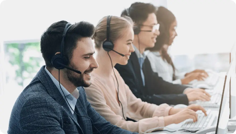 Four helpdesk workers smiling whilst working wearing headphones in front of computers